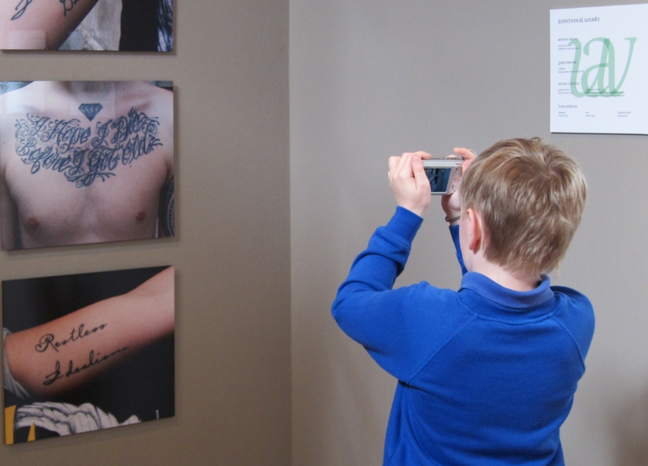 A child in a blue school jumper taking a photo of an art exhibit
